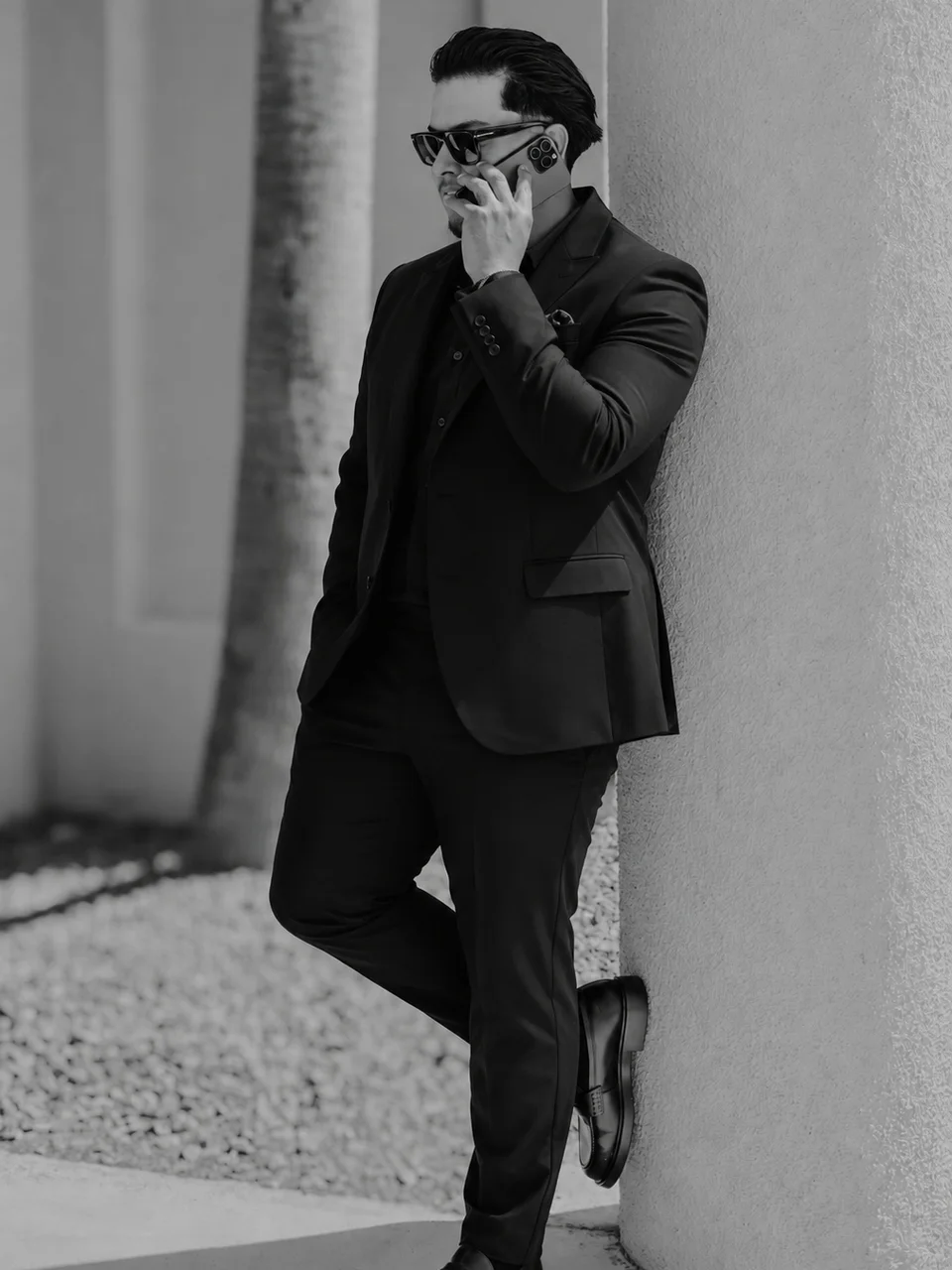 Jesse Ramos in a black suit taking a call, leaning against a column in the desert sun