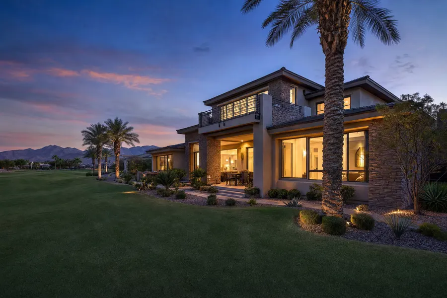 Two-story home on a golf course fairway at dusk with palm trees