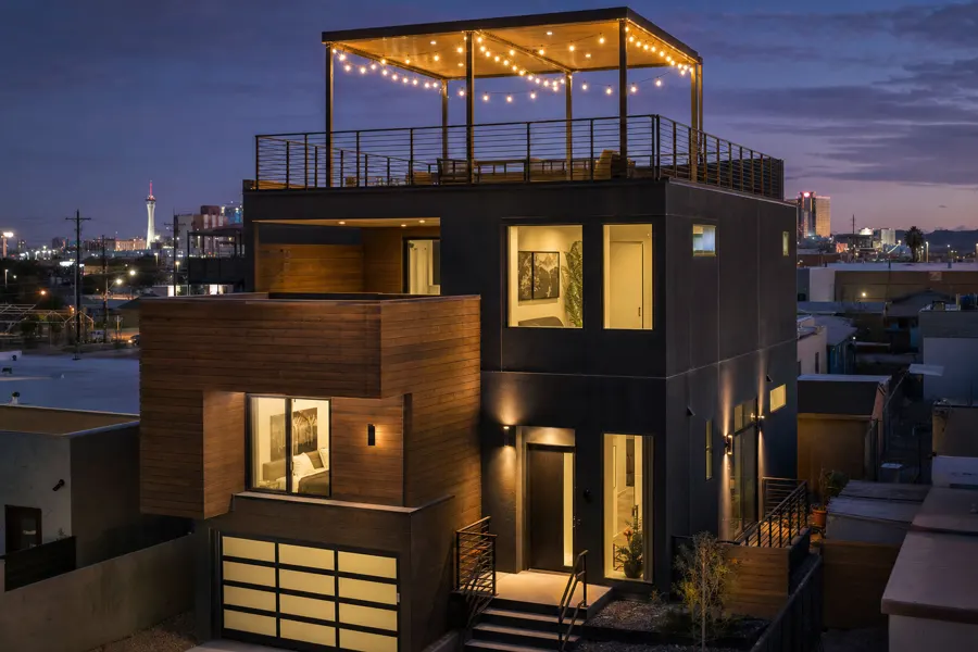 Modern dark-clad urban townhome with rooftop deck and city lights behind
